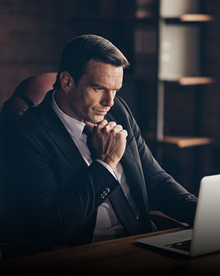 A professional man in a suit sitting at a desk, focused on his laptop - The Law Offices Of Matthew Cargal