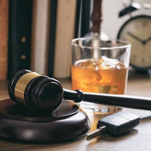 A gavel and a glass of wine on a desk, accompanied by car keys and a clock, symbolizing a DUI trial in California. - The Law Offices Of Matthew Cargal